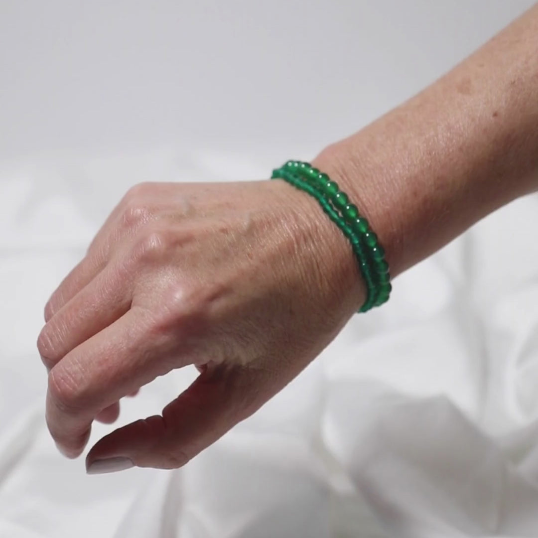 a woman wearing two green onyx stone bracelets on her arm