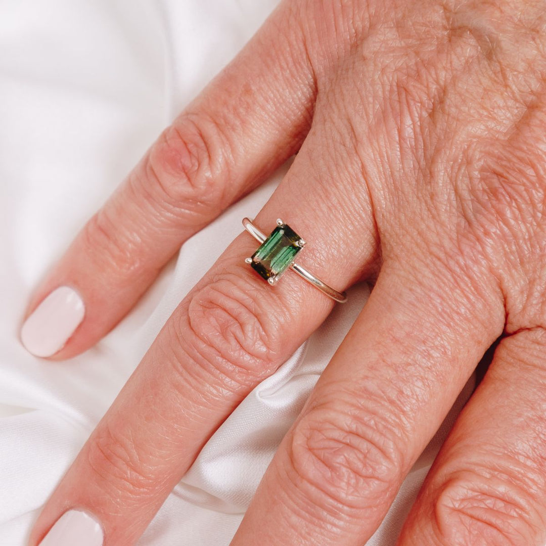 a woman wearing a gemstone ring on her finger 