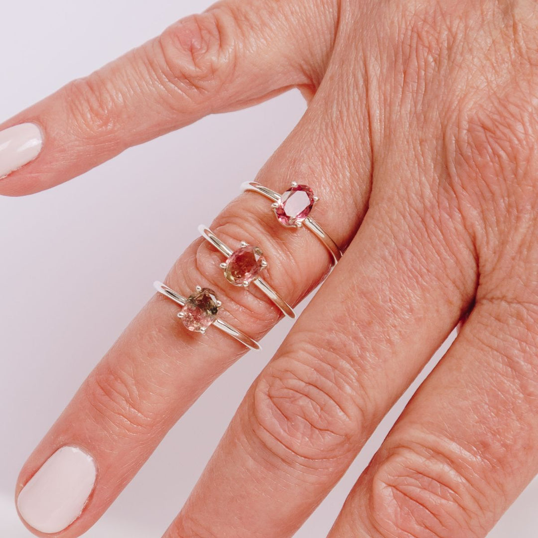 a woman wearing three oval shaped gemstone rings on her finger