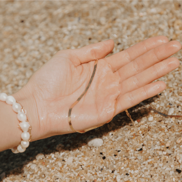 hand holding herringbone necklace over sea sand 